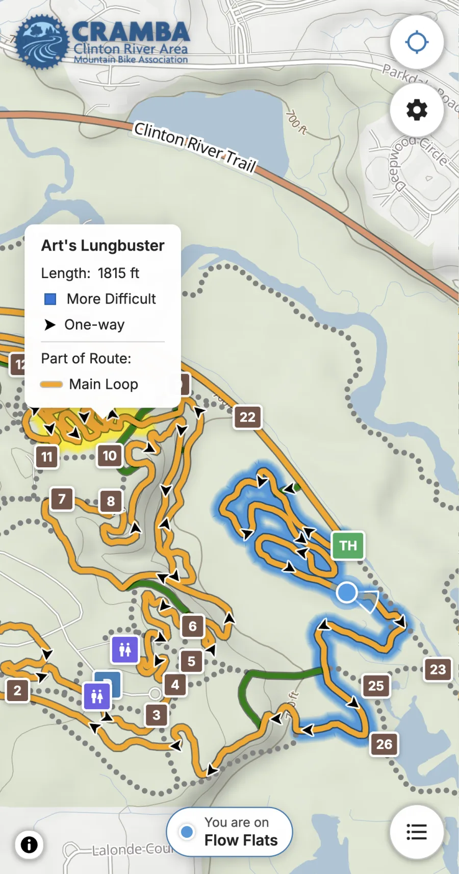 A trailmaps.app map open on a phone at Bloomer Park. The rider's position is on Flow Flats, which glows blue, with a cone showing the direction they face and a label at the bottom naming the trail. A card shows the details for Art's Lungbuster.